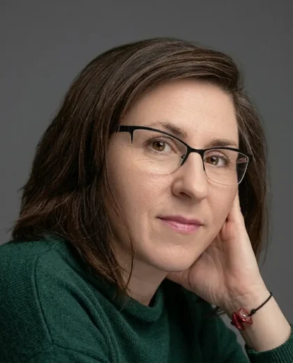 Portret kobiety w okularach i ciemnozielonej bluzce, przedstawiający architekta wnętrz Małgorzatę Mierzwińską.