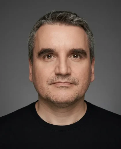 Portret mężczyzny z krótkimi ciemnymi włosami na neutralnym tle, przedstawiający wizualizatora 3D Sebastiana Mierzwinskiego.